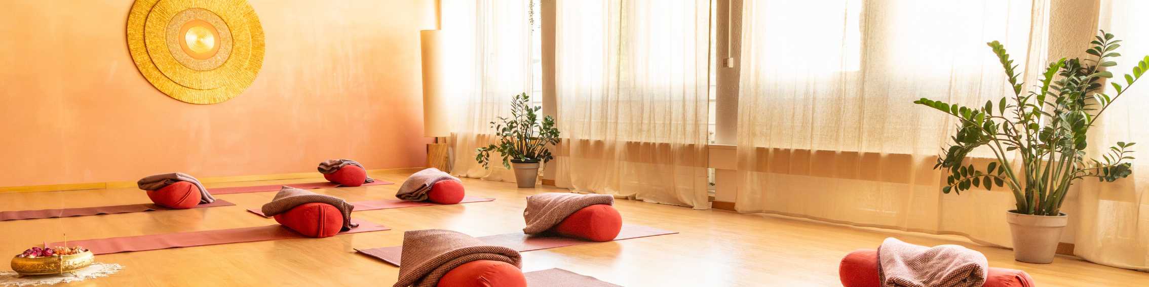 Ein heller Raum mit Yogamatten und gelben Vorhängen.
