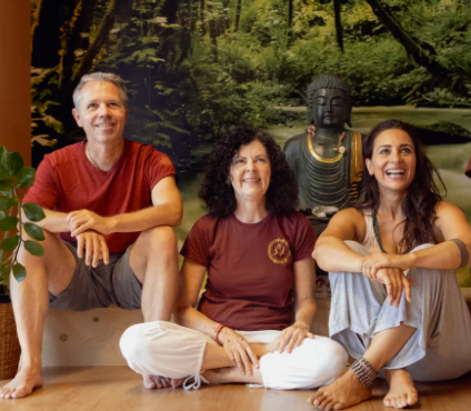 Eine Gruppe von drei Menschen sitzt vor einer Buddha-Statue.